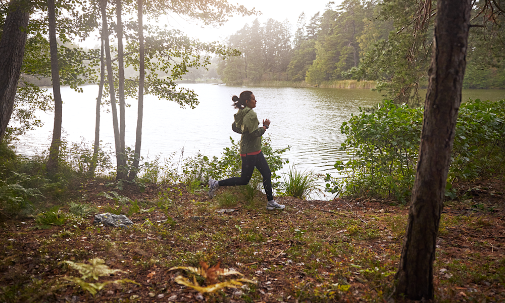 Tjej med smartklocka och träningskläder springer i skogen