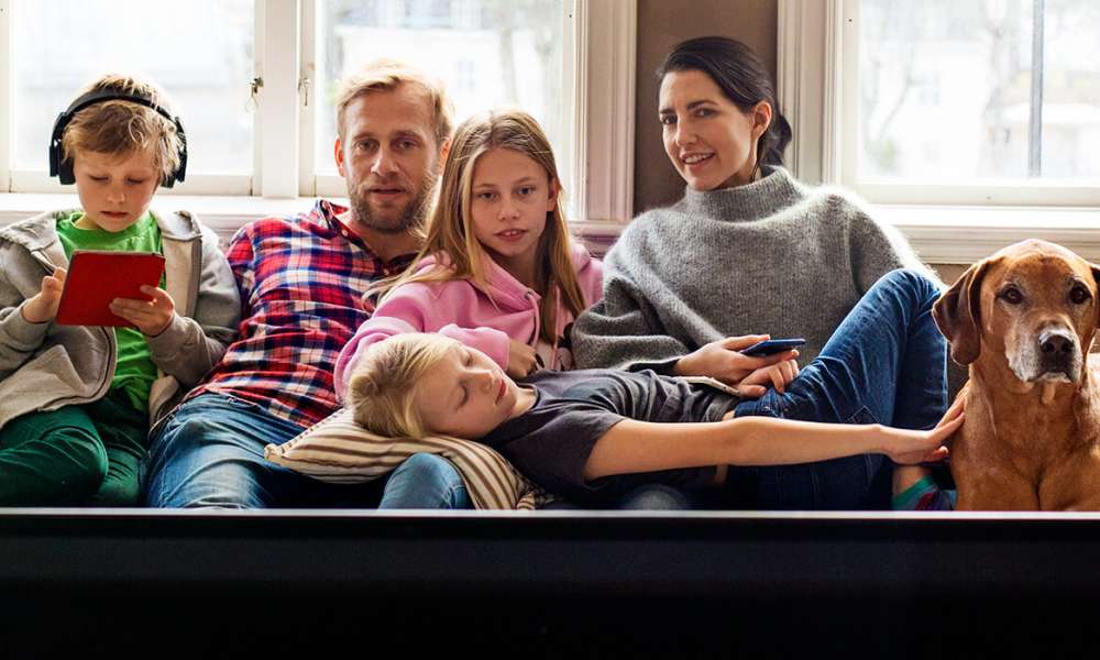 Familj med tre barn och hund samlad i tv-soffan.