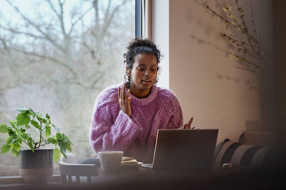 Kvinna i stickad tröja sitter framför datorn i hemmiljö