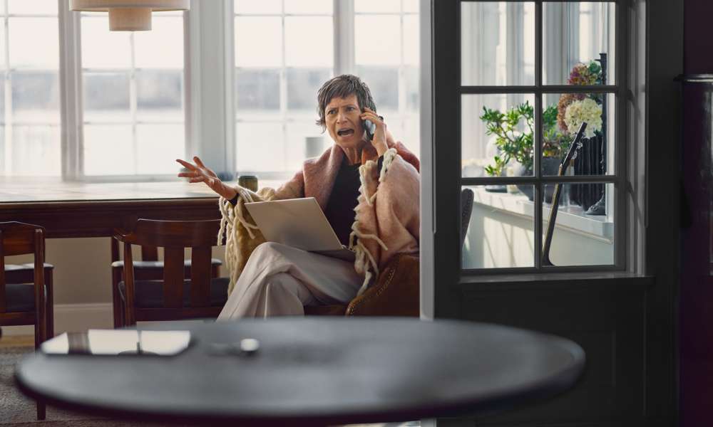 Äldre kvinna talar i mobiltelefon med ett upprört ansiktsuttryck.