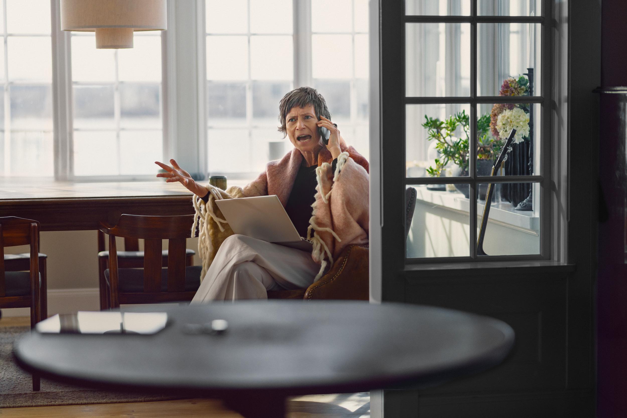 Äldre kvinna talar i mobiltelefon med ett upprört ansiktsuttryck.