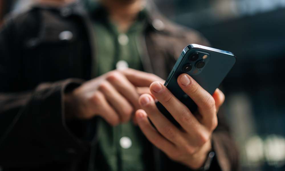 Närbild på en mans händer som använder en mobiltelefon.