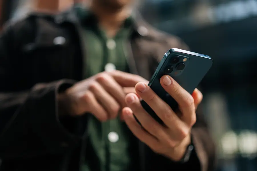 Närbild på en mans händer som använder en mobiltelefon.
