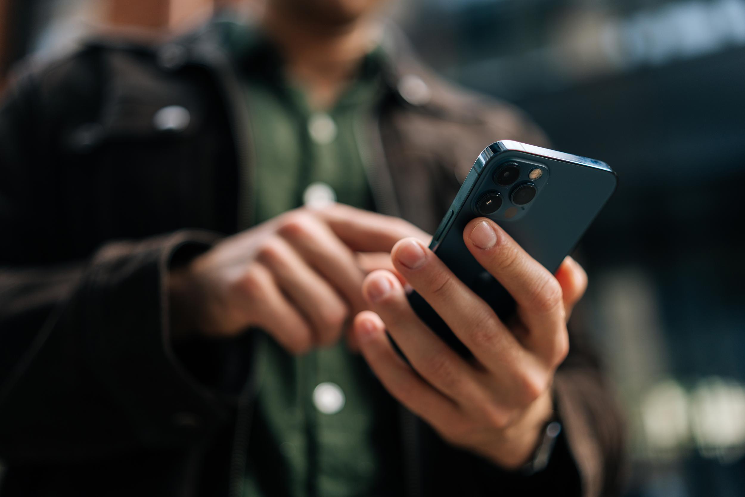 Närbild på en mans händer som använder en mobiltelefon.