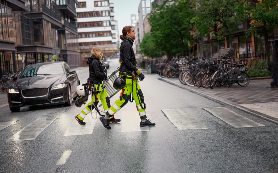 Manlig och kvinnlig byggare går över övergångsställe med stege.