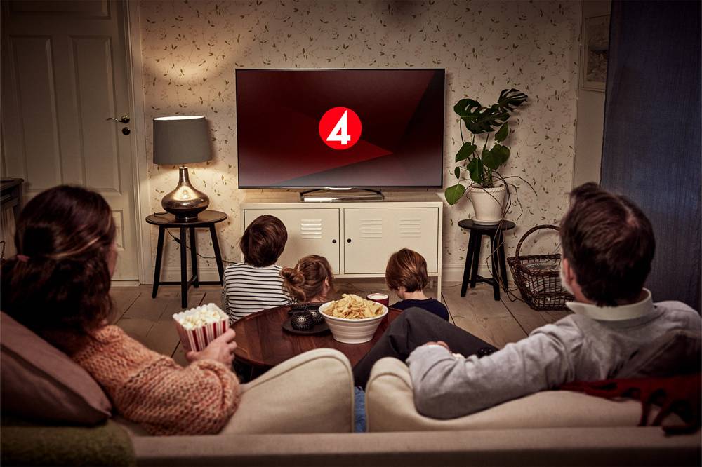En familj sitter i soffan och tittar på tv med TV4:s logotyp i bild. 