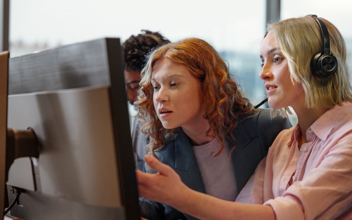 Unga kollegor på kontor, man och två kvinnor, kollar uppmärksamt på datorskärm.