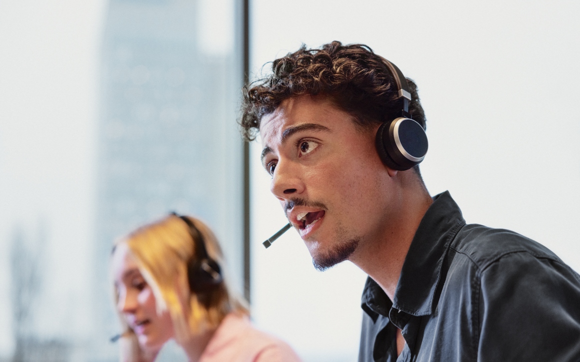 Ung man och kvinna med headset arbetar med IT-support på kontor.