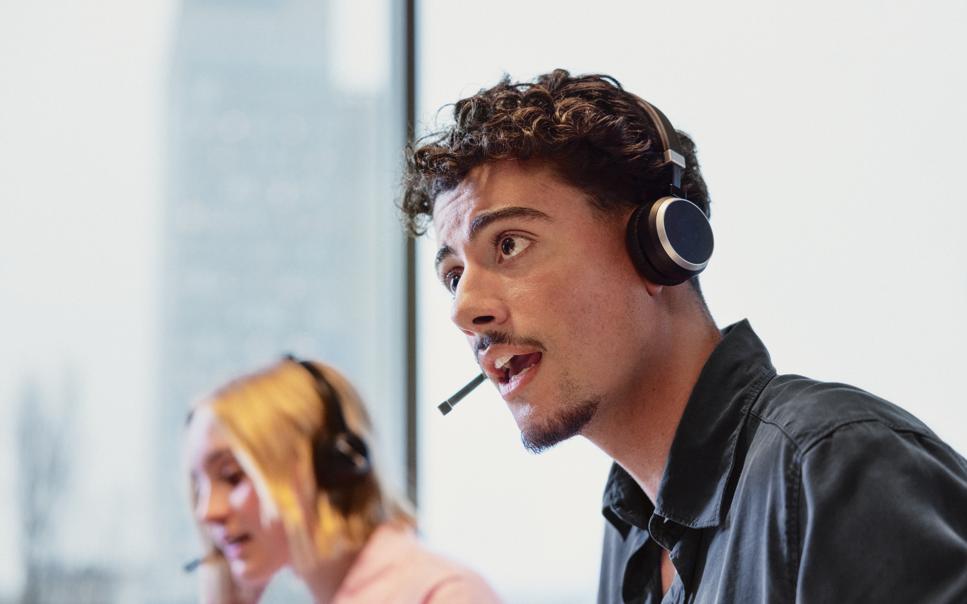 Ung man och kvinna med headset arbetar med IT-support på kontor.