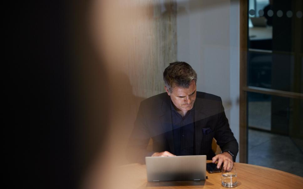 Man med laptop och mobil sitter vid skrivbord.