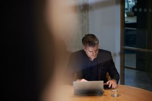 Man med laptop och mobil sitter vid skrivbord.