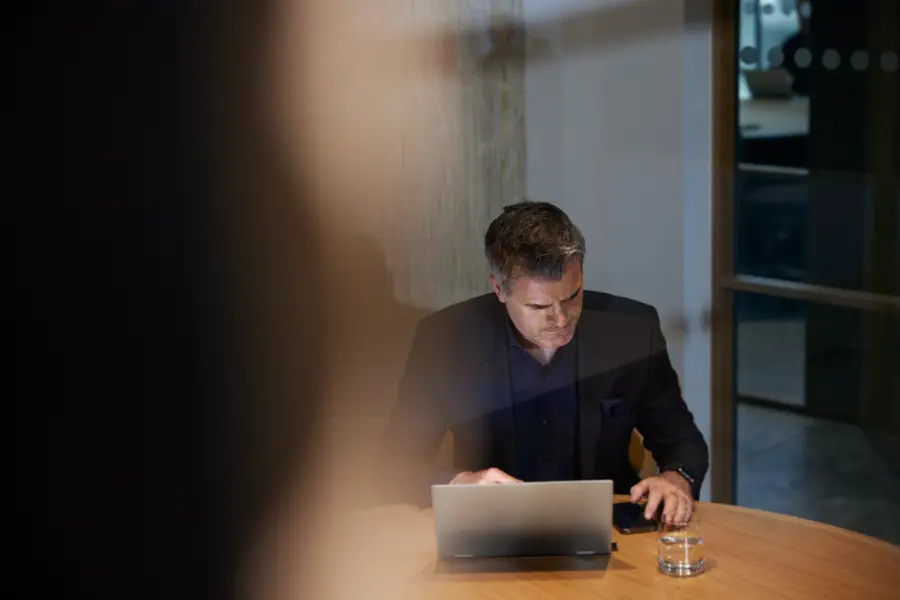 Man med laptop och mobil sitter vid skrivbord.