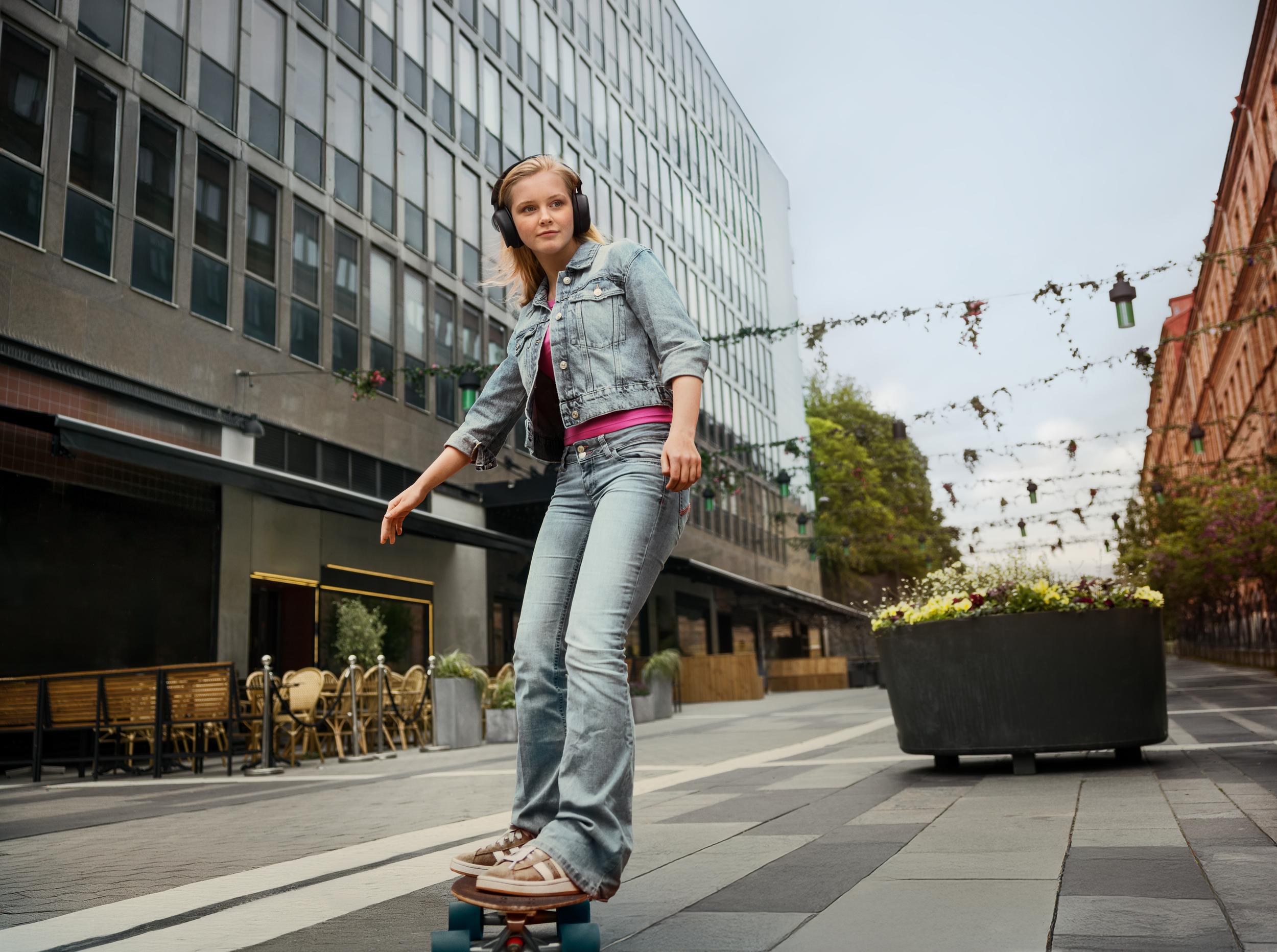 Tjej med hörlurar på skateboard i stadsmiljö
