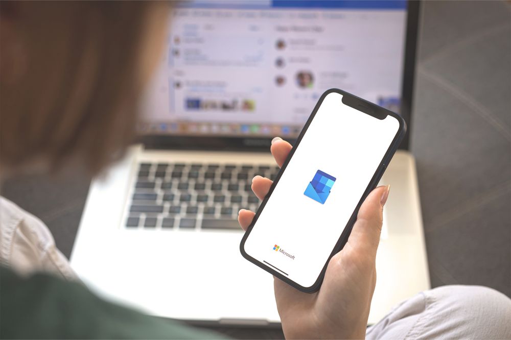 Kvinna håller i mobil med Outlook, laptop med Microsoft 365 i bakgrunden.