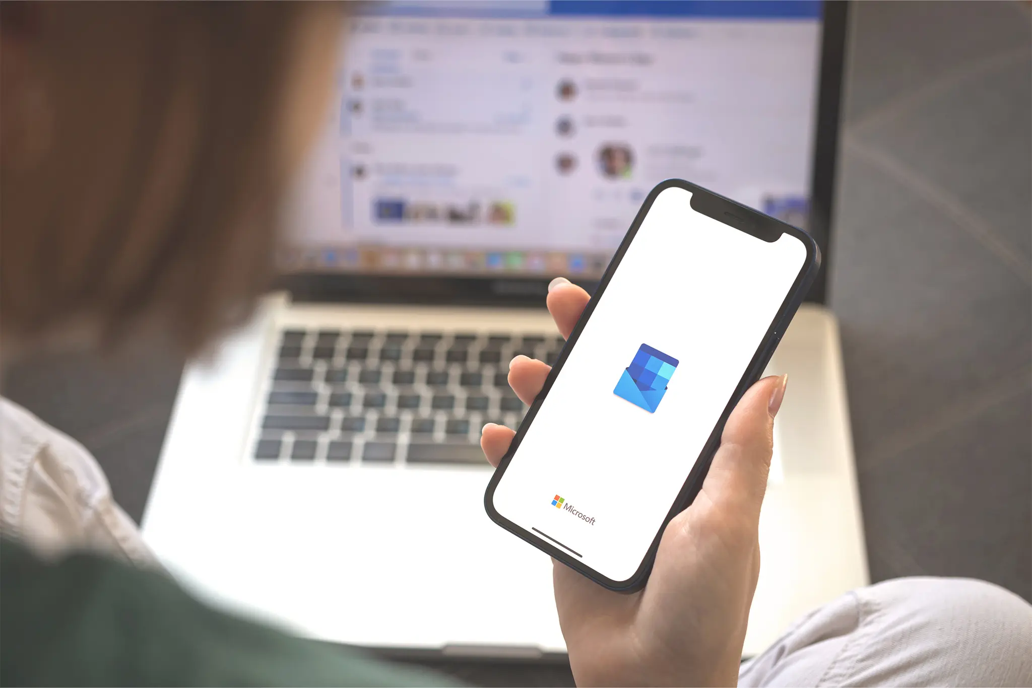 Kvinna håller i mobil med Outlook, laptop med Microsoft 365 i bakgrunden.