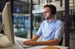 Man med headset och skjorta framför dator på kontor.