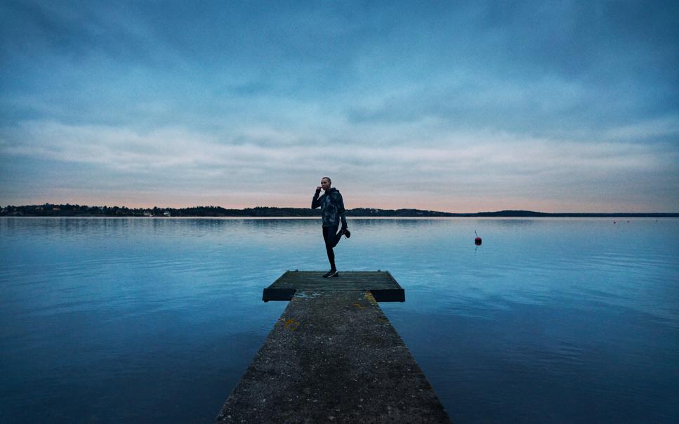Man stretchar på brygga och pratar i mobiltelefon på kvällen.