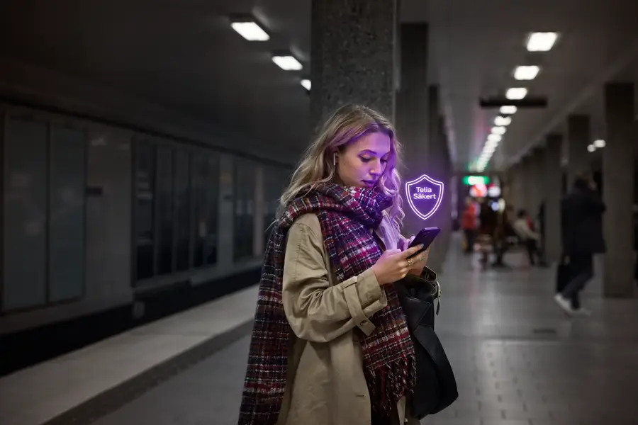 En kvinna står i tunnelbanan och tittar på sin mobil, med den lila säkerhetsskölden.