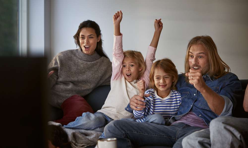Familj med mamma, pappa och två barn sitter framför tv:n och hejar på sitt lag. Upptäck tv och streaming från Telia.