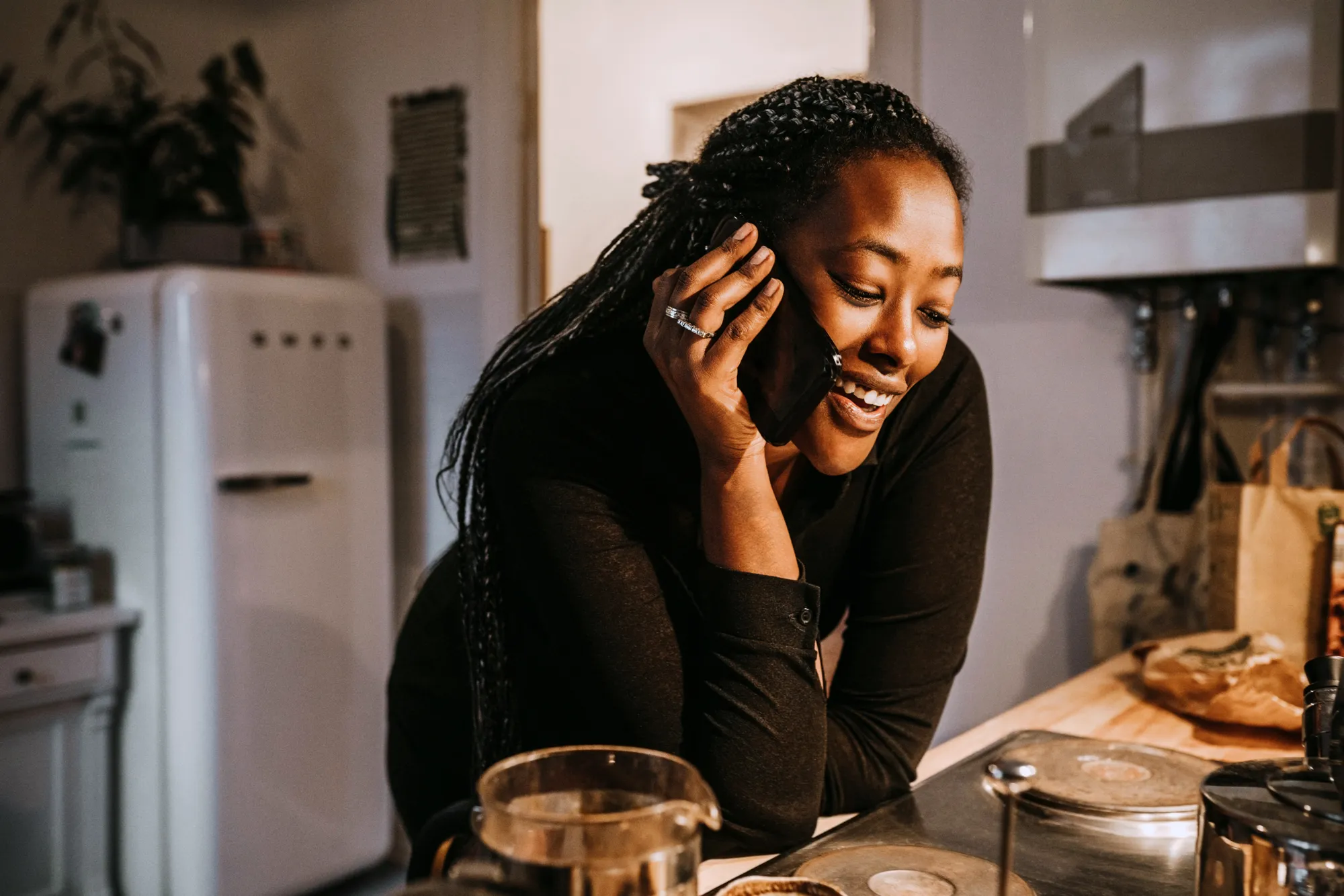 Kvinna som står vid spisen i köket och pratar i sin telefon och ler.