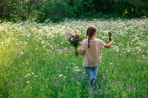 Barn i en grönskande blomsteräng som håller en bukett blommor i ena handen och en mobil i andra.