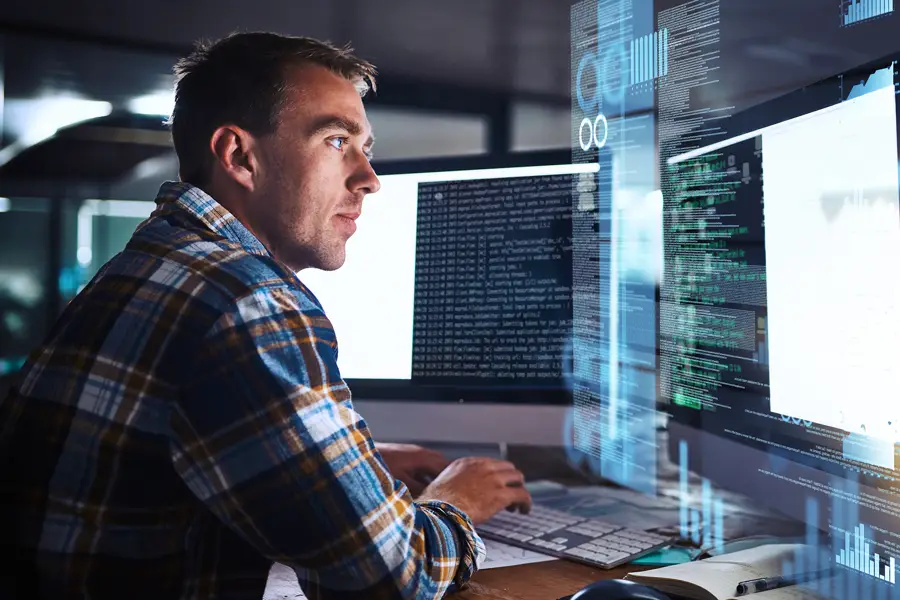 IT-tekniker sitter framför skärmar i flanellskjorta på kontor.
