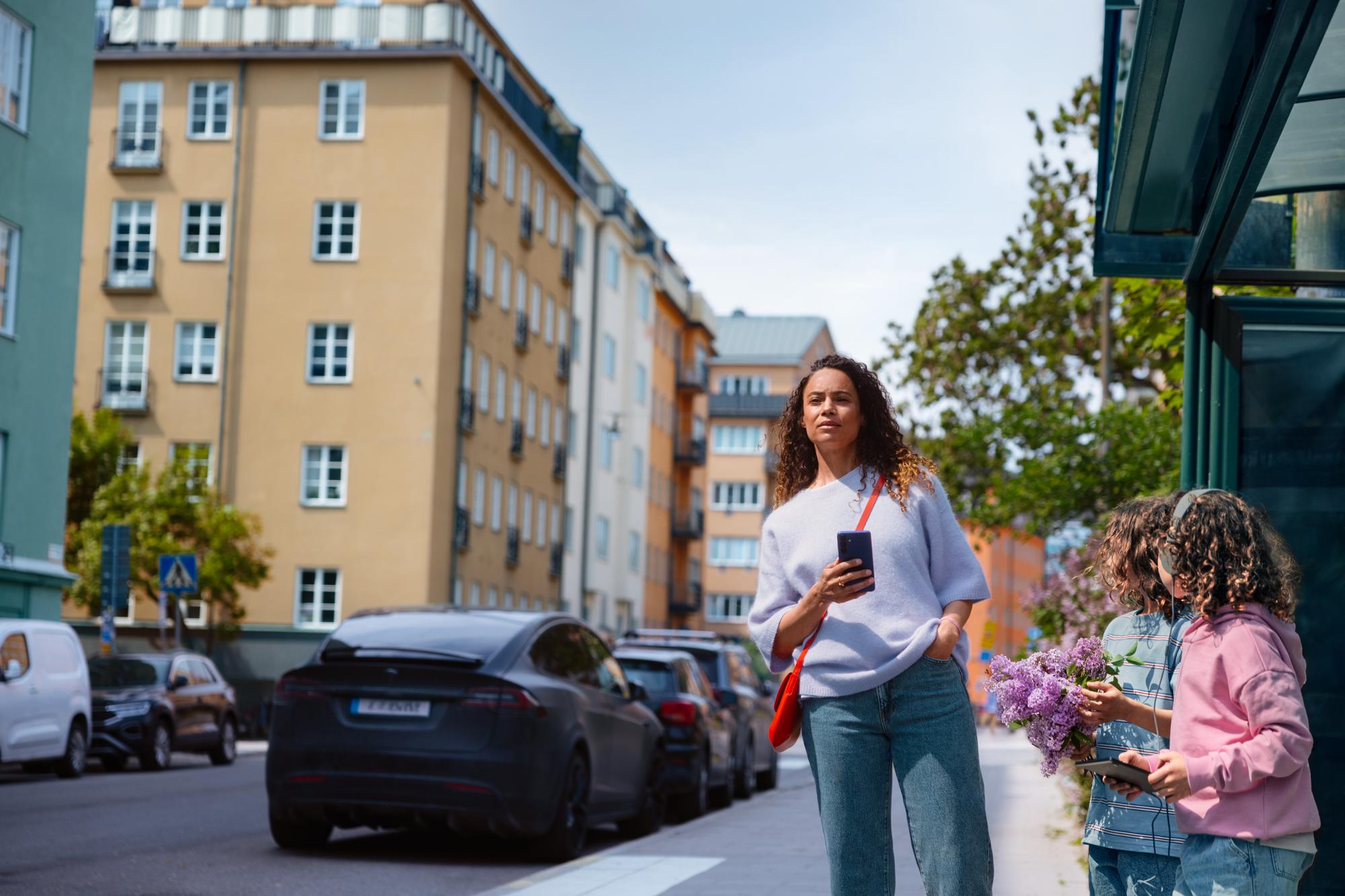 Kvinna vid bushållsplats håller i mobil