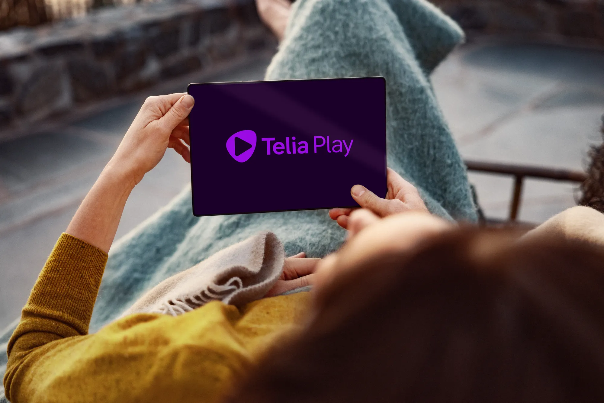 Person lutar sig tillbaka och tittar på Telia Play på sin surfplatta. Streama allt på ett och samma ställe, direkt i Telia Play-appen.