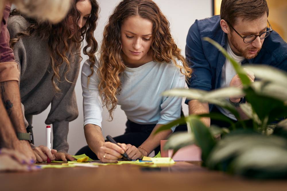 Kollegor skriver på post its under workshop på kontor.