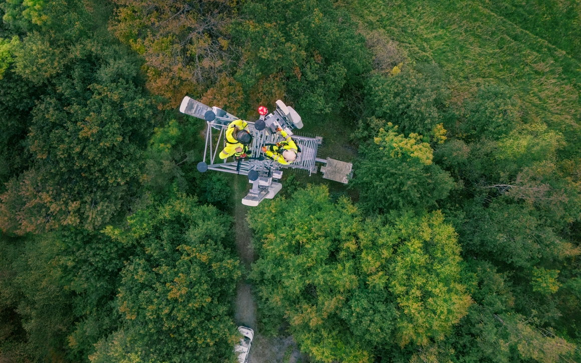 Arbetare i gula säkerhetskläder uppe i telemast i skogsmiljö