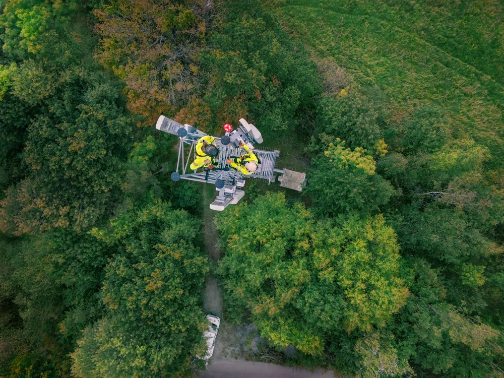 Arbetare i gula säkerhetskläder uppe i telemast i skogsmiljö