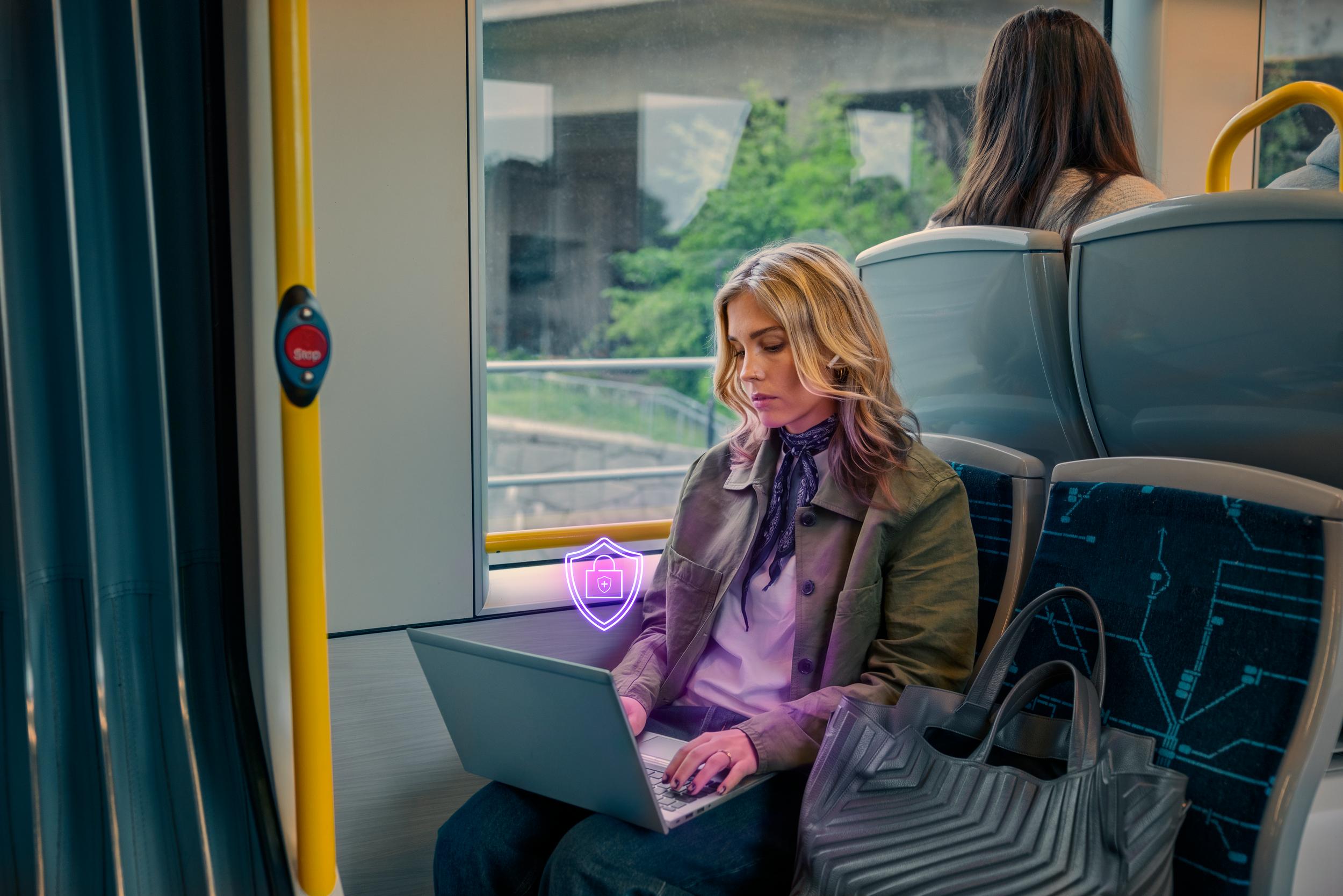 Kvinna sitter på tvärbana med laptop med säkerhetslogga