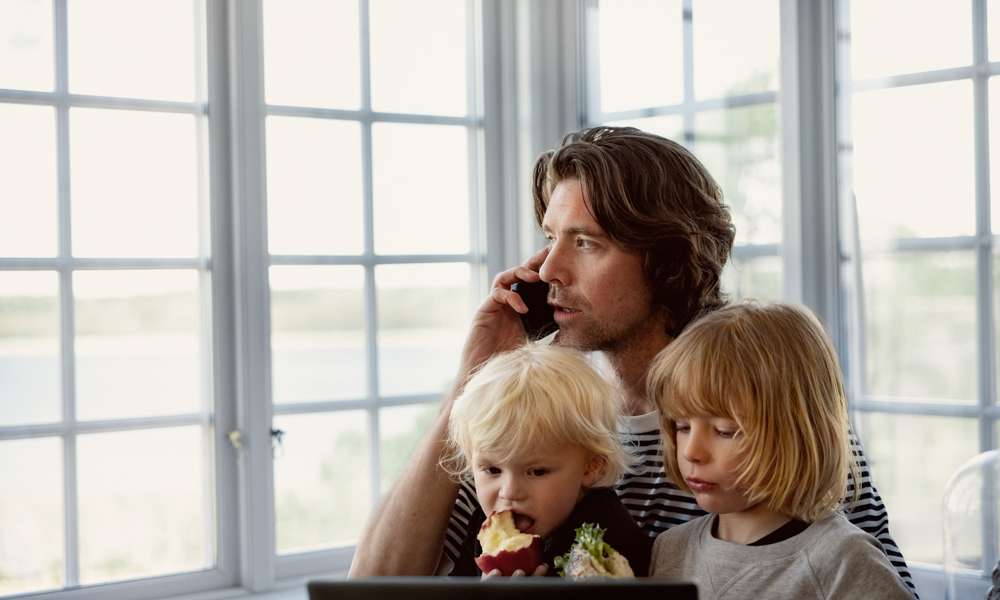 Man med småbarn i knät talar i mobil hemma