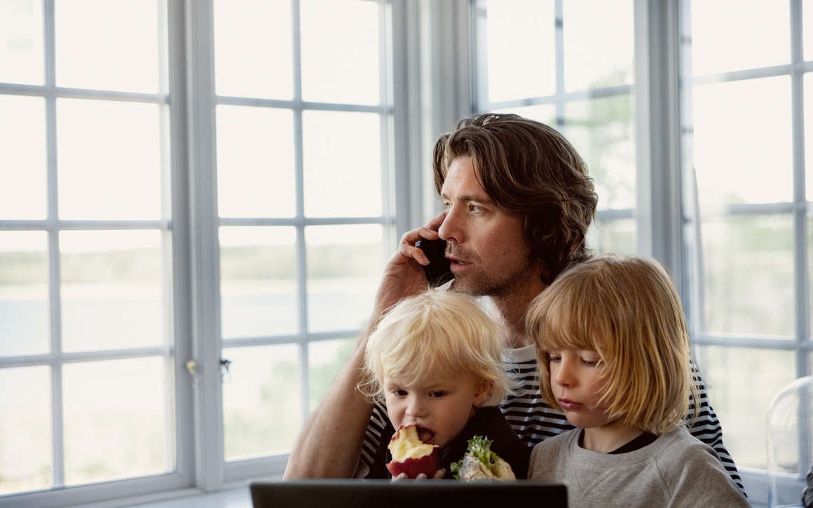 Man med småbarn i knät talar i mobil hemma