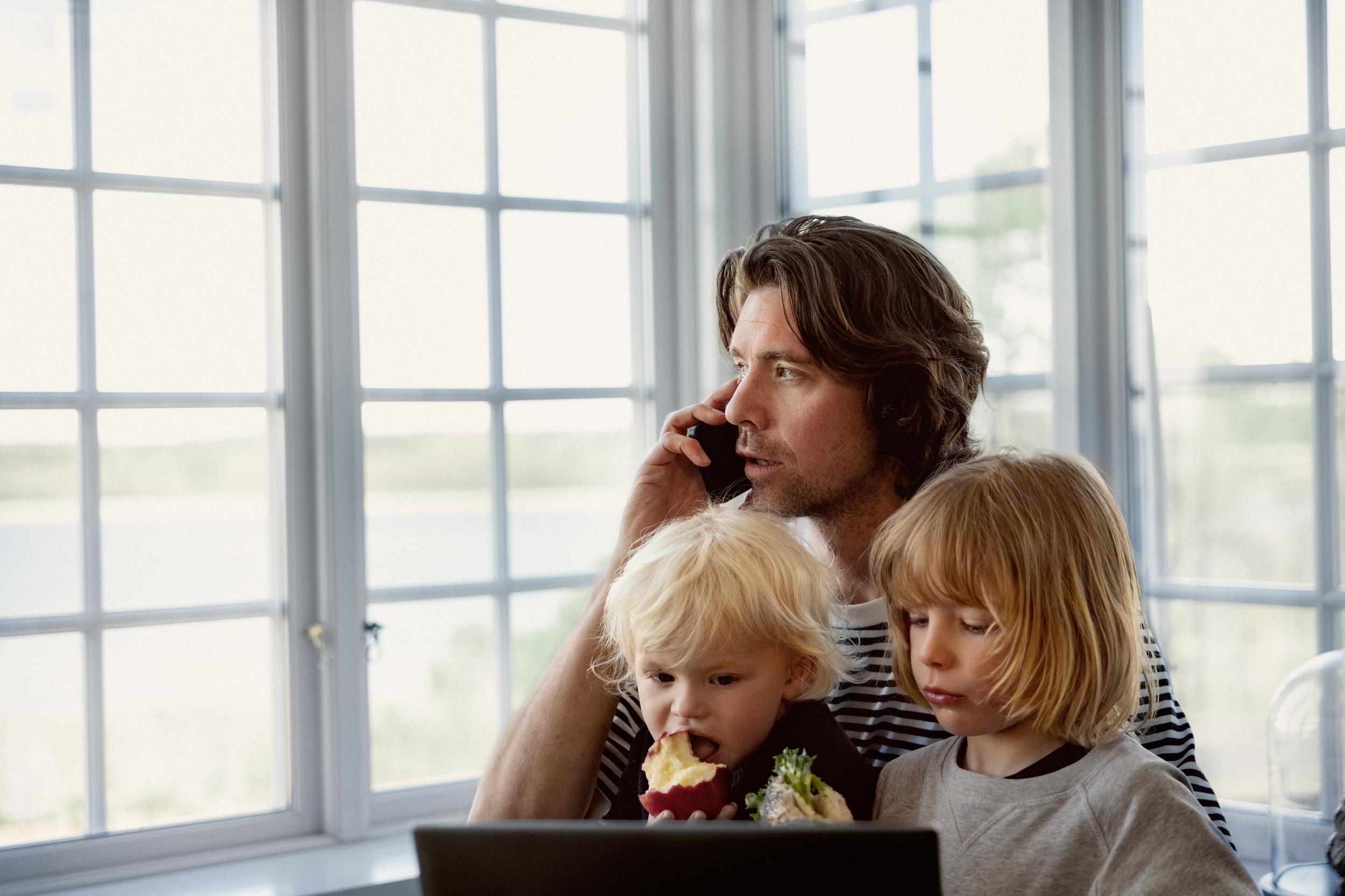Man med småbarn i knät talar i mobil hemma