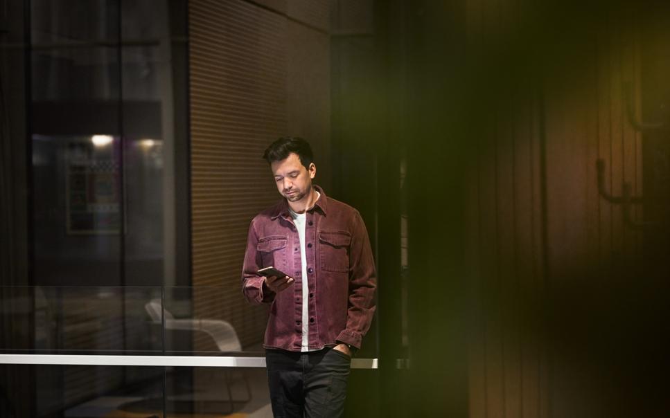 Avslappnat klädd man håller i telefon med företagsabonnemang på kontor.