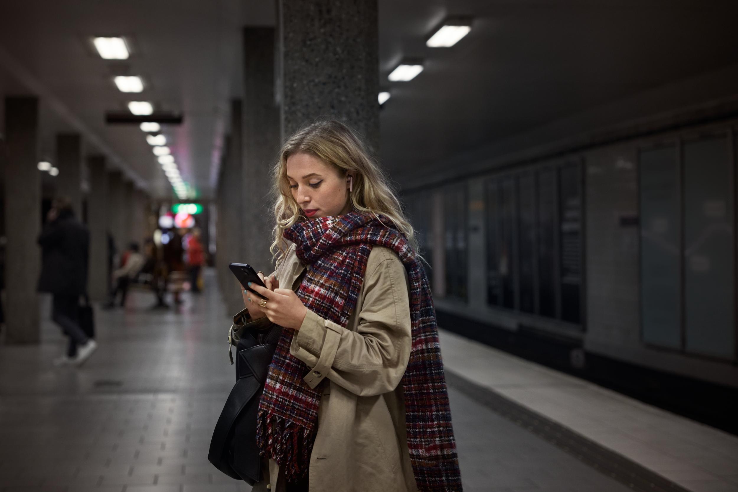 Kvinna tittar på mobiltelefon på perrong i tunnelbanan