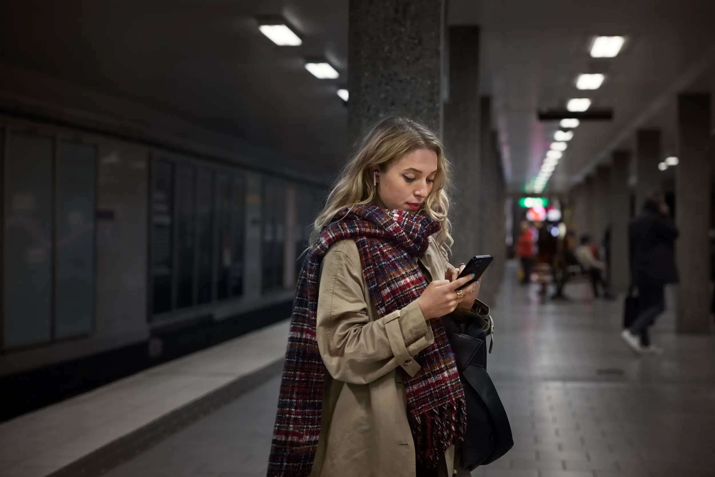 Kvinna tittar på mobiltelefon på perrong i tunnelbanan