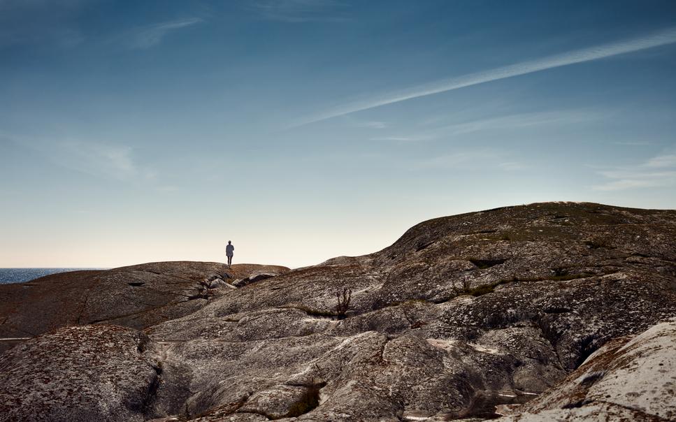 Person standing on a round rock formation in a natural landscape.