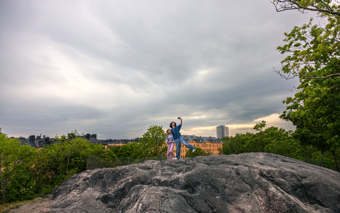 Två personer tar selfie på klippor med Stockholm stad i bakgrunden.