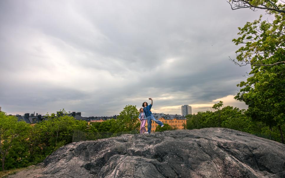 Två personer tar selfie på klippor med Stockholm stad i bakgrunden.
