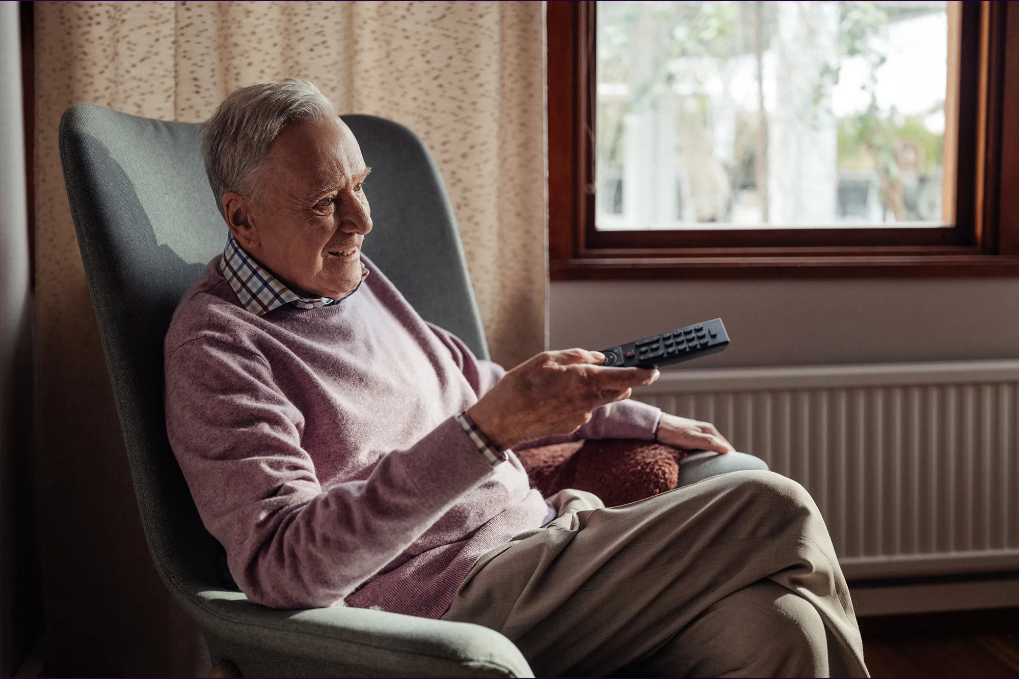 Telia-pappan som sitter i fåtöljen med en fjärrkontroll i handen och tittar på tv och ler.