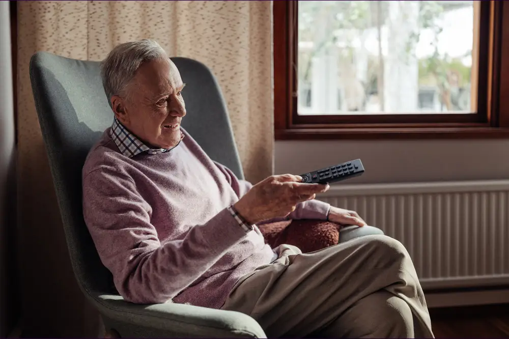 Telia-pappan som sitter i fåtöljen med en fjärrkontroll i handen och tittar på tv och ler.