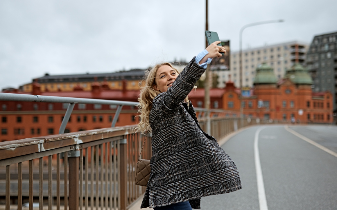 Kvinna i rutig jacka står utomhus på en bro och tar en selfie