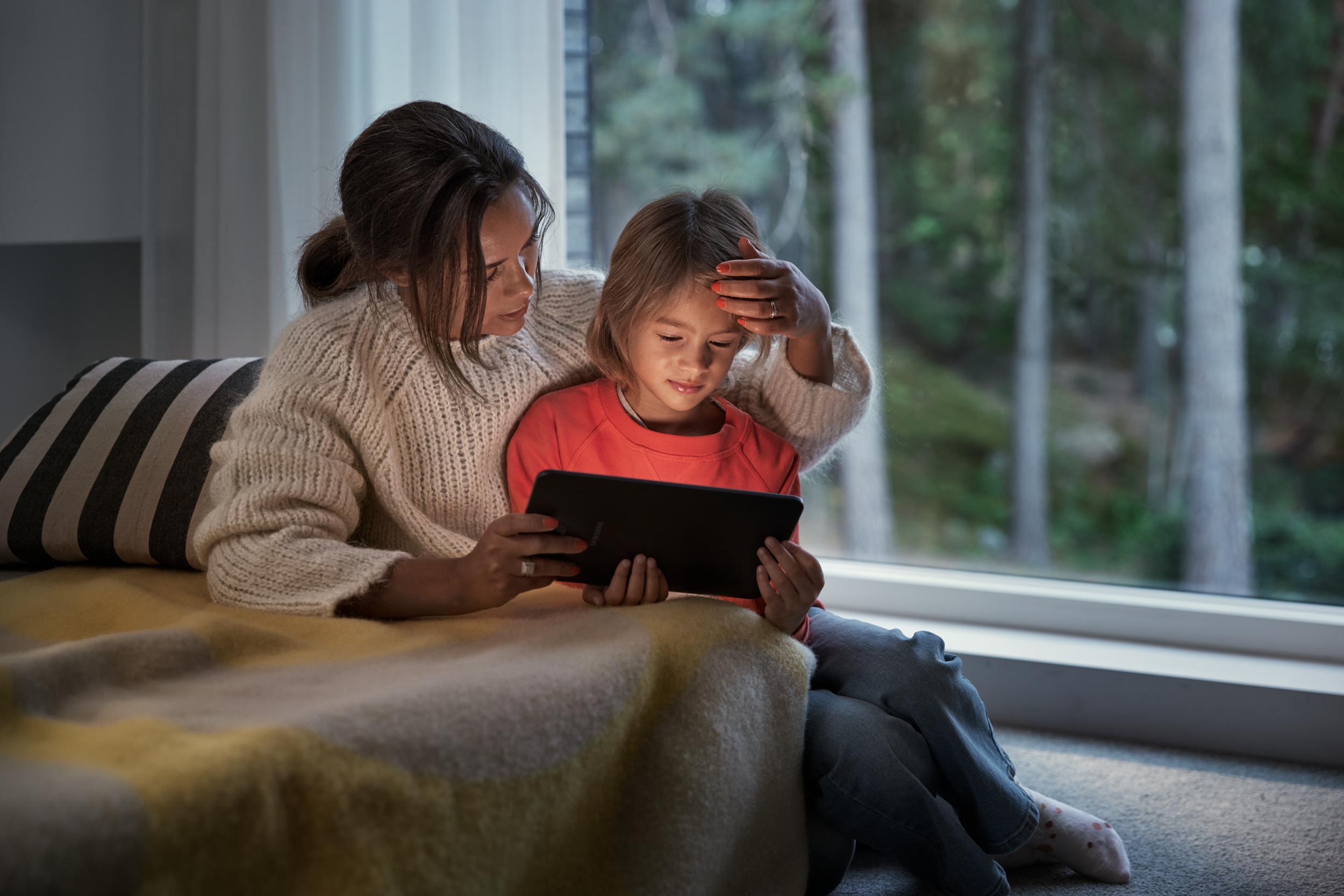 Mamma och pojke tittar på surfplatta i soffan.