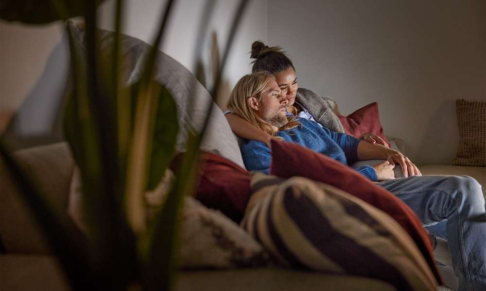 Ett yngre par sitter tillsammans i soffan och tittar på tv.