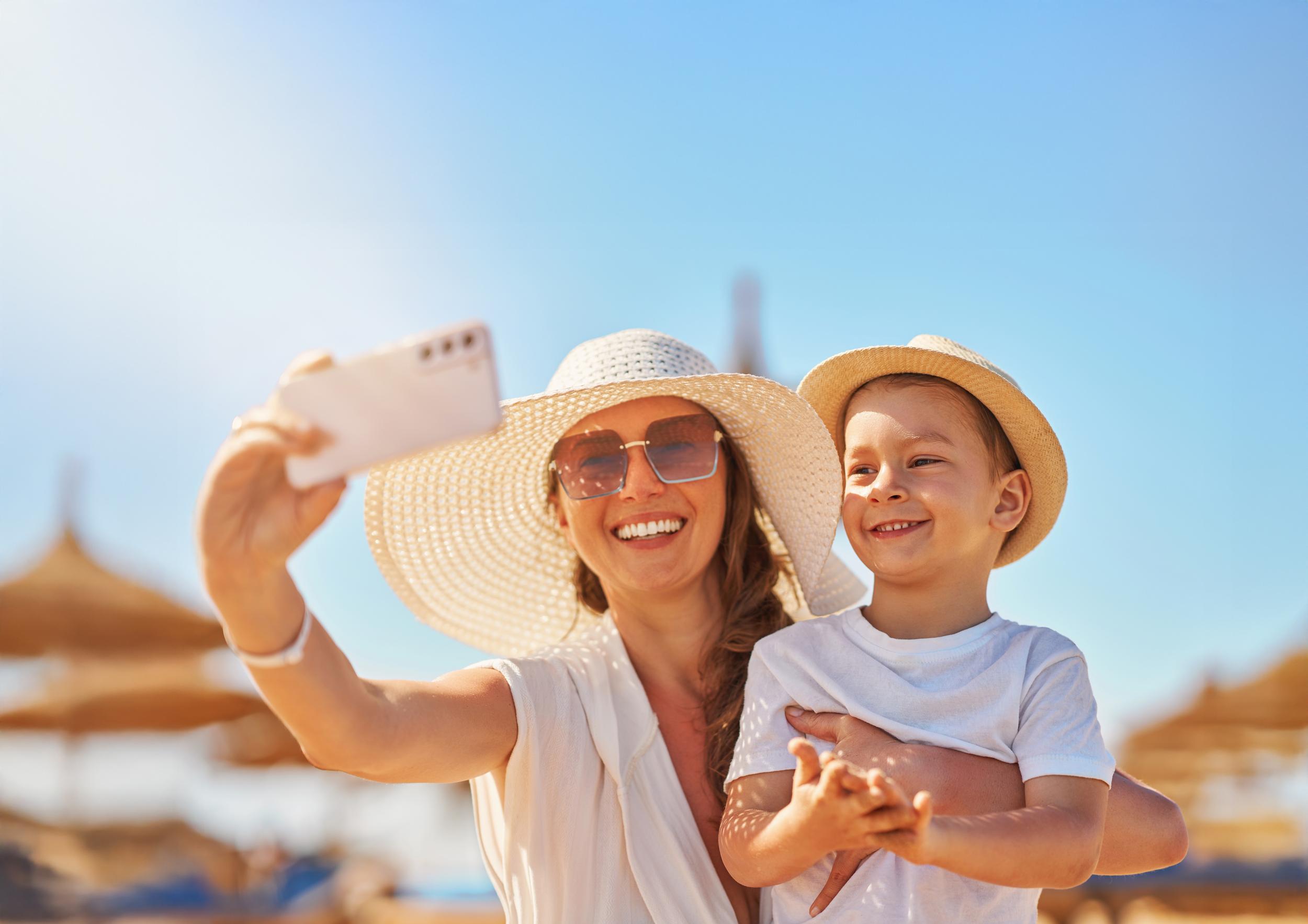 Kvinna i solhatt och pojke tar selfie på semester med parasoll i bakgrunden