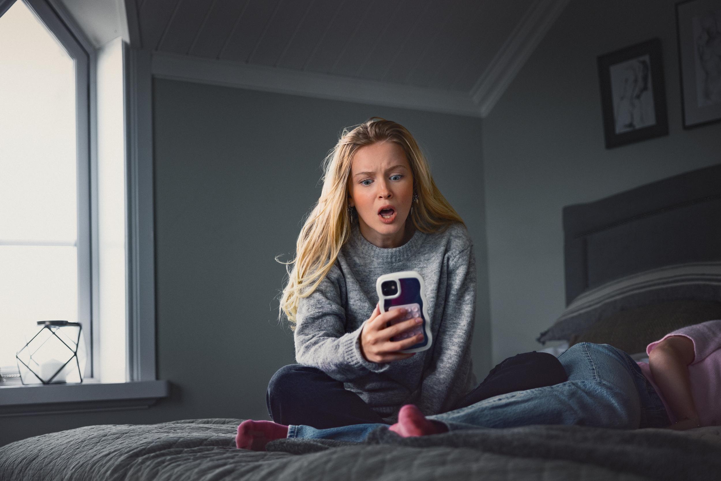 Kvinna tittar på sin mobil med oroligt ansiktsuttryck.