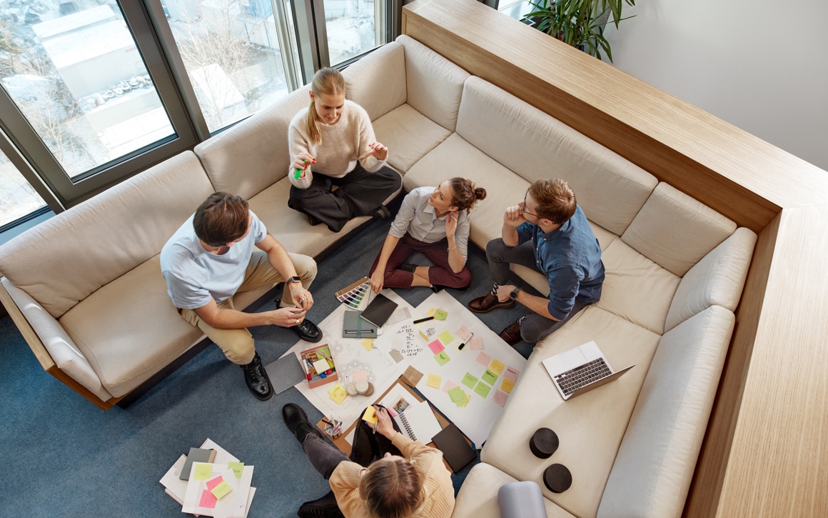 Kollegor har workshop i soffa med laptops och post-its på kontor.