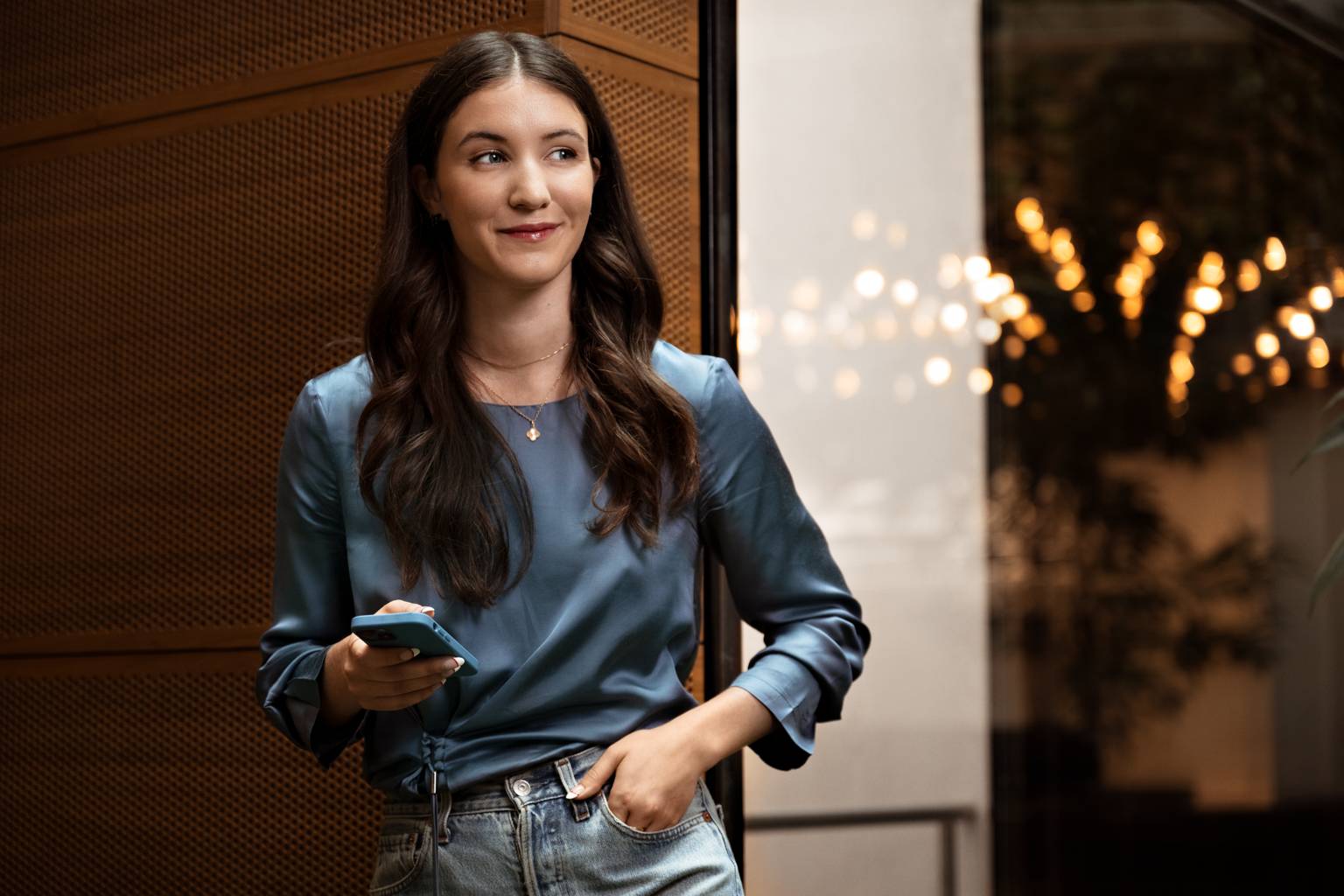 Kvinna i blå tröja står med sin mobil och tittar ut i rummet